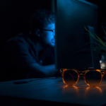 Pessoa trabalhando no computador com exposição à luz azul e óculos de bloqueio